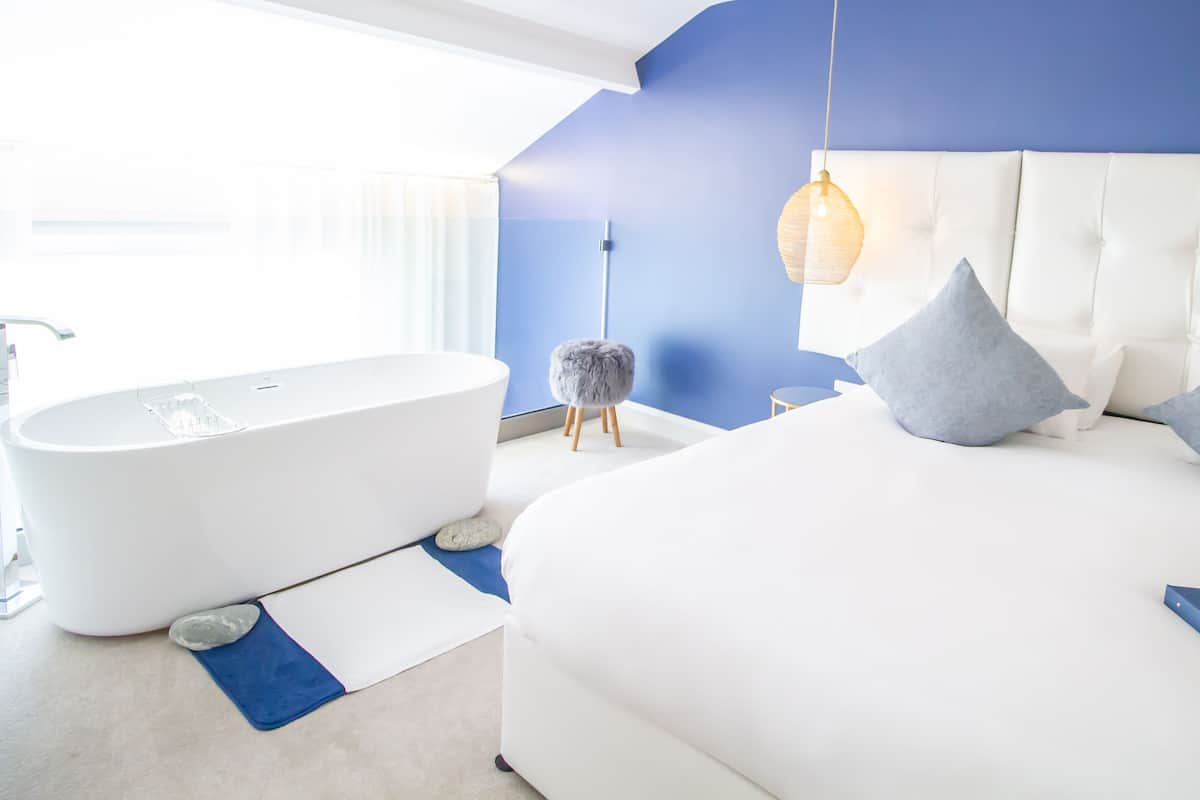 A modern bedroom with a large bed, a white headboard, and a blue accent wall.