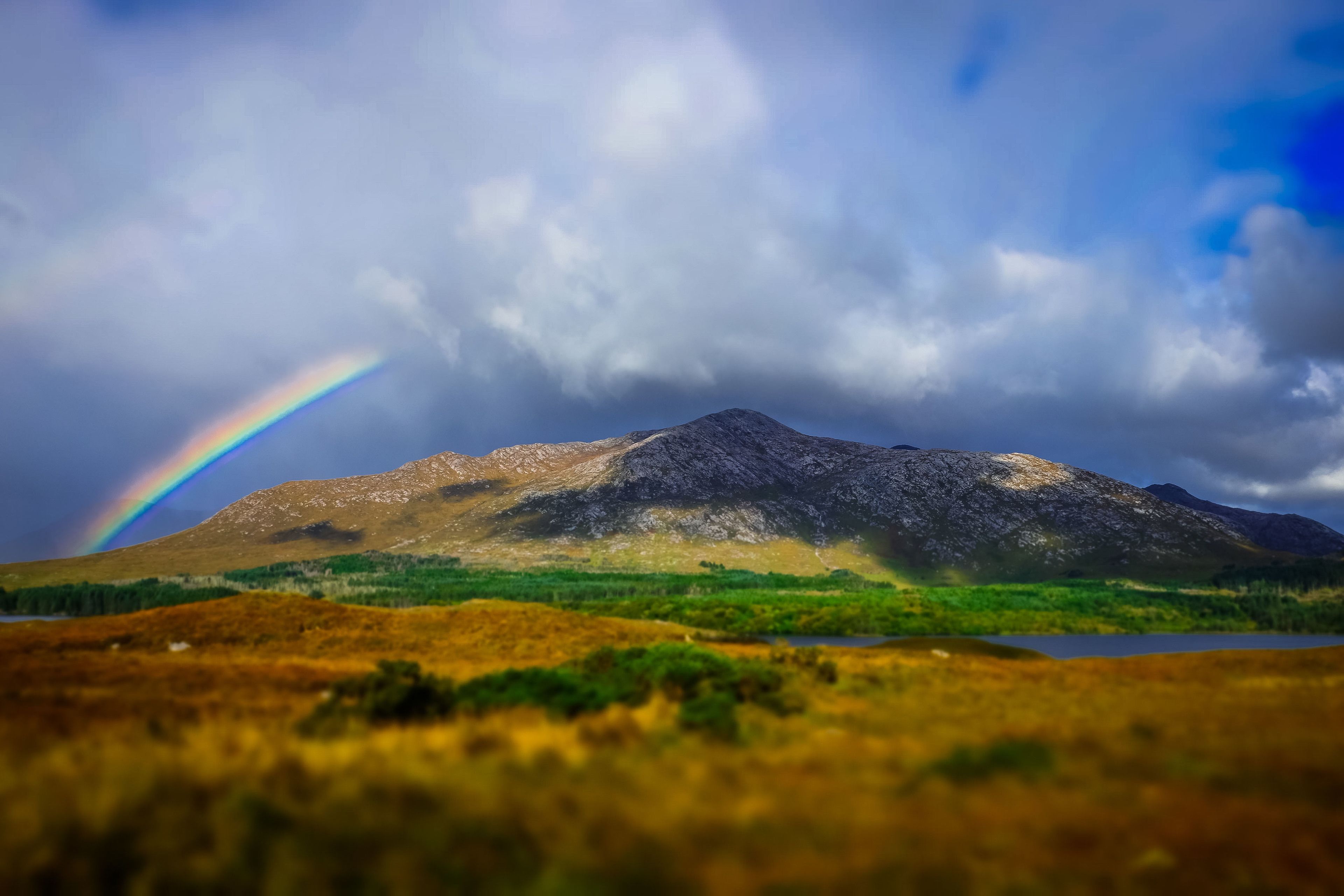A mountain with a rainbow, a lake, and a grassy foreground.