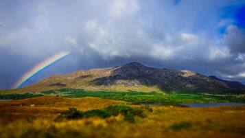 A mountain with a rainbow, a lake, and a grassy foreground.