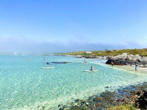 A coastal scene with clear turquoise water, rocky shoreline, and a few people engaging in water activities.