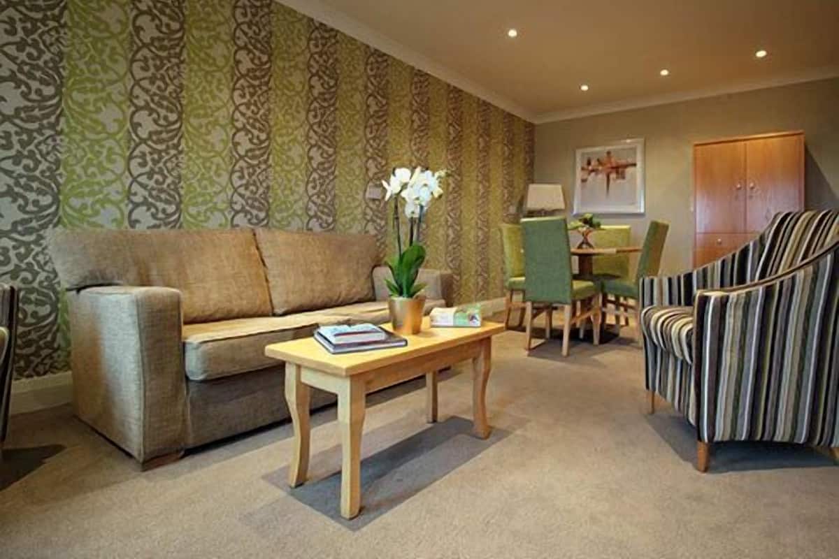A living room with a sofa, a striped armchair, a small table with a book and a vase of flowers.