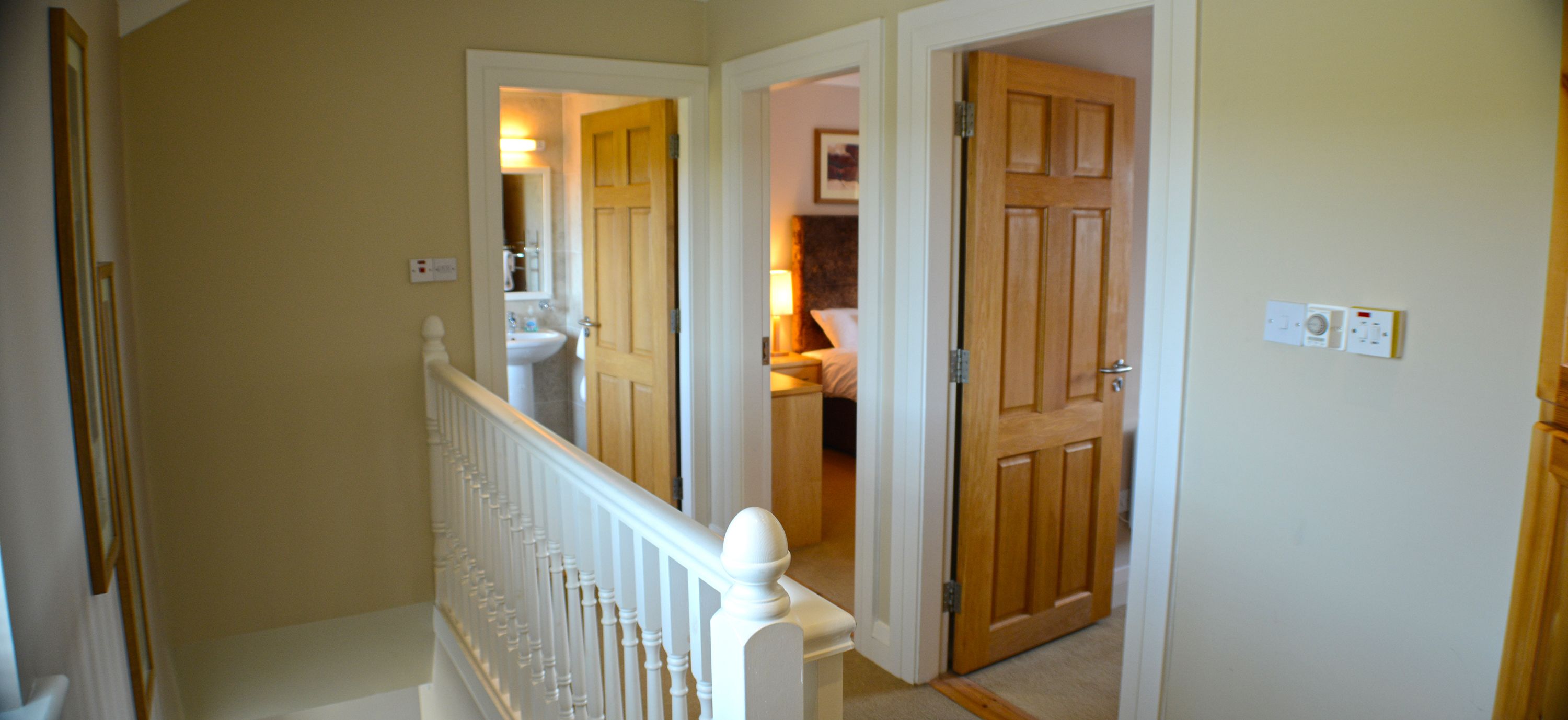 A hallway with a white railing, a wooden door, and a light switch on the wall.