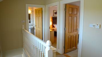 A hallway with a white railing, a wooden door, and a light switch on the wall.