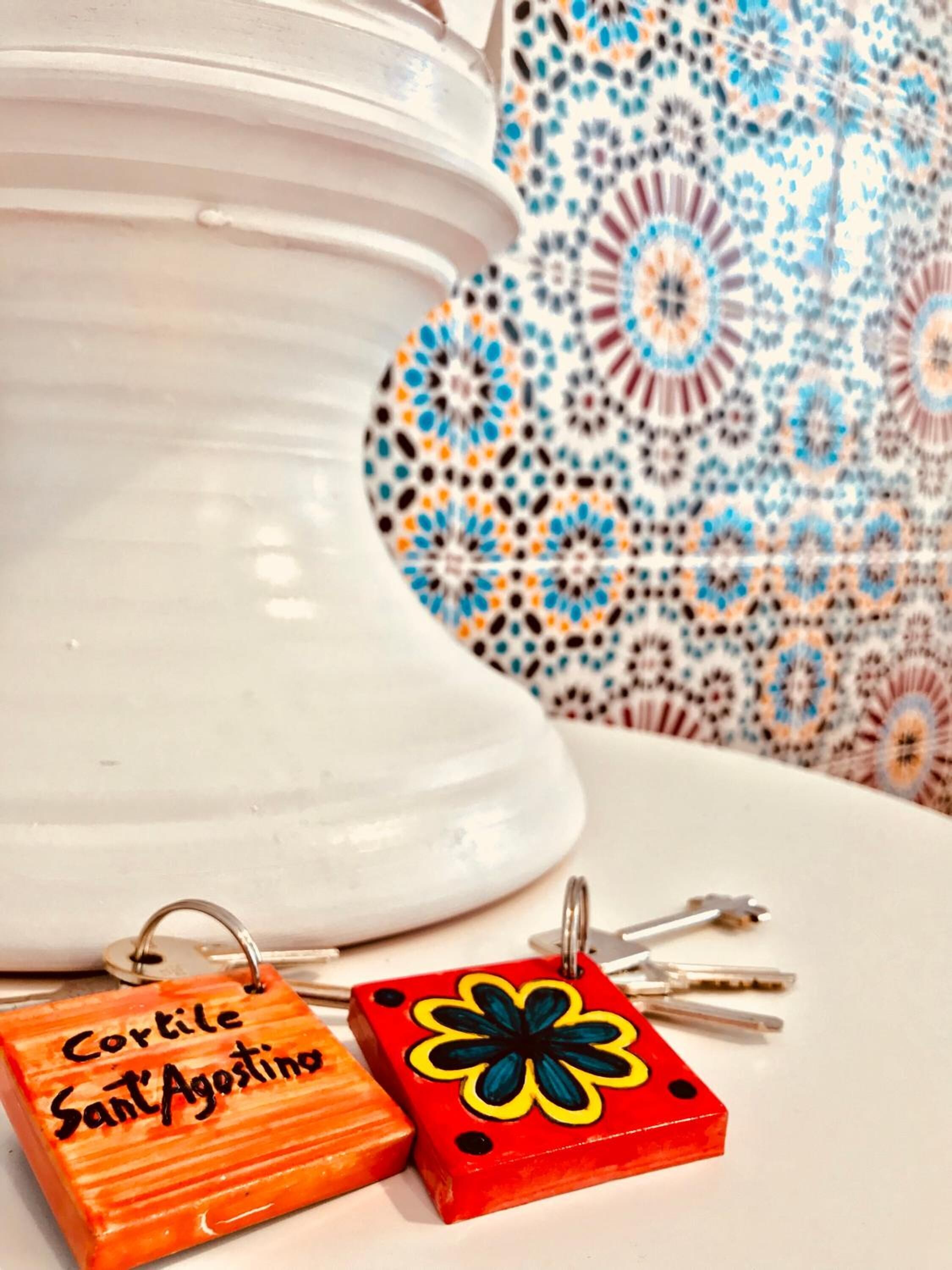 A white ceramic vase with a floral pattern in the background and two keychains with inscriptions.