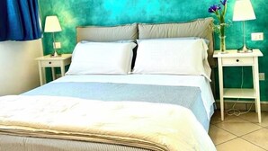 Ein Bett mit blau-weiß gestreifter Bettdecke, zwei weiße Nachttische mit Lampen und eine wandfarbene Wand in Türkis.