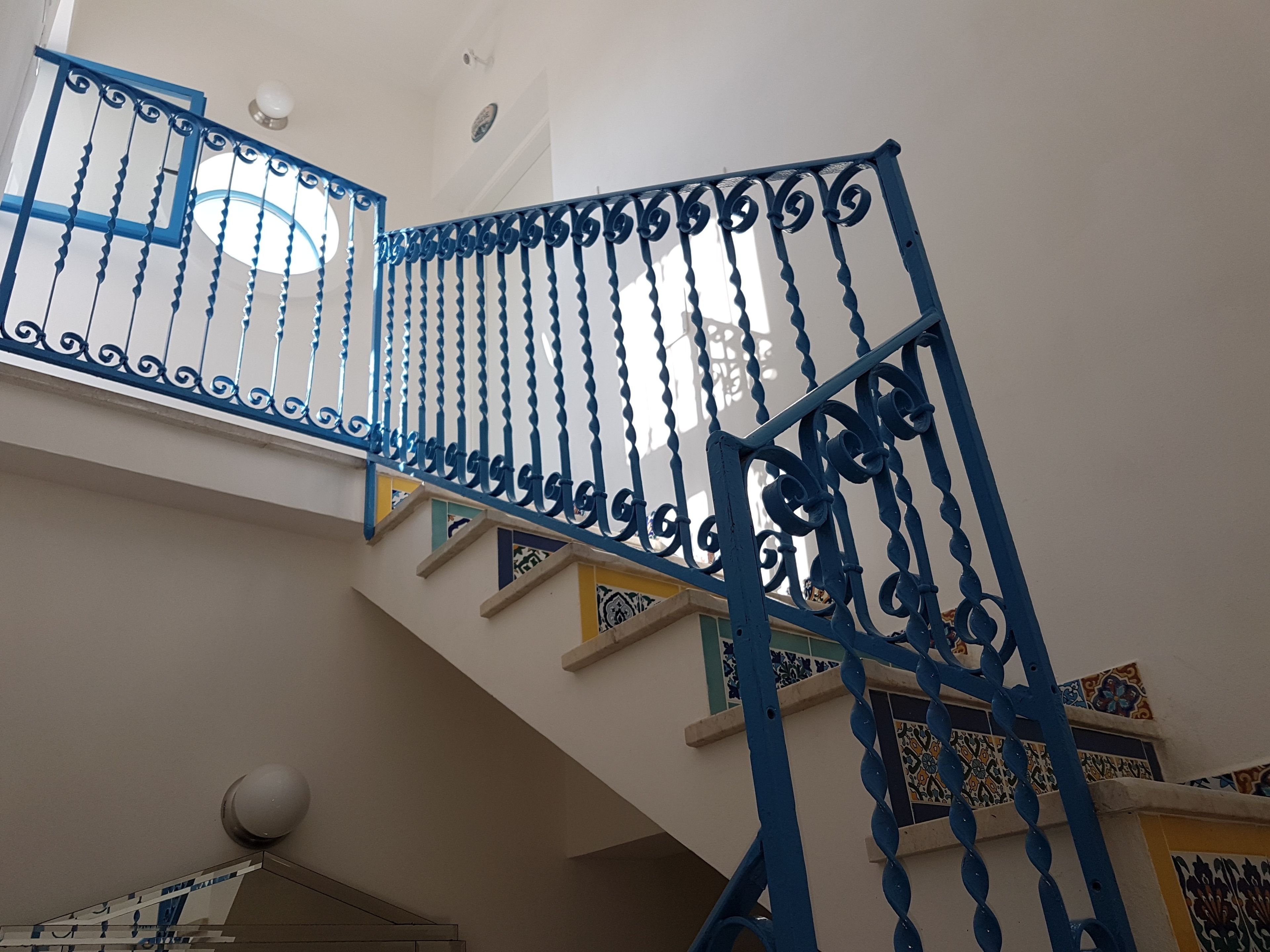 A staircase with blue metal railings and patterned tiles on the walls.