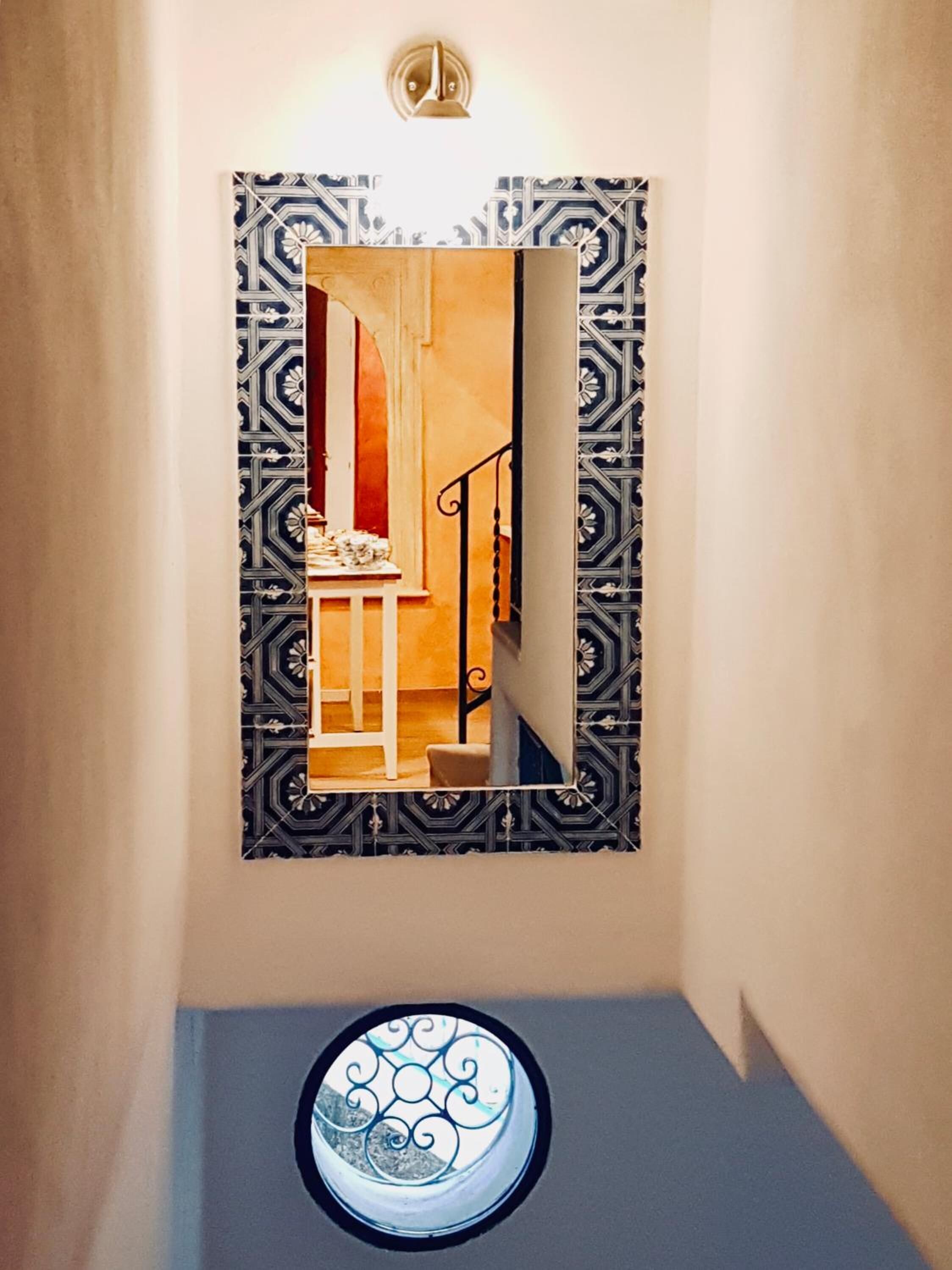 A hallway with a decorative mirror and a circular window.