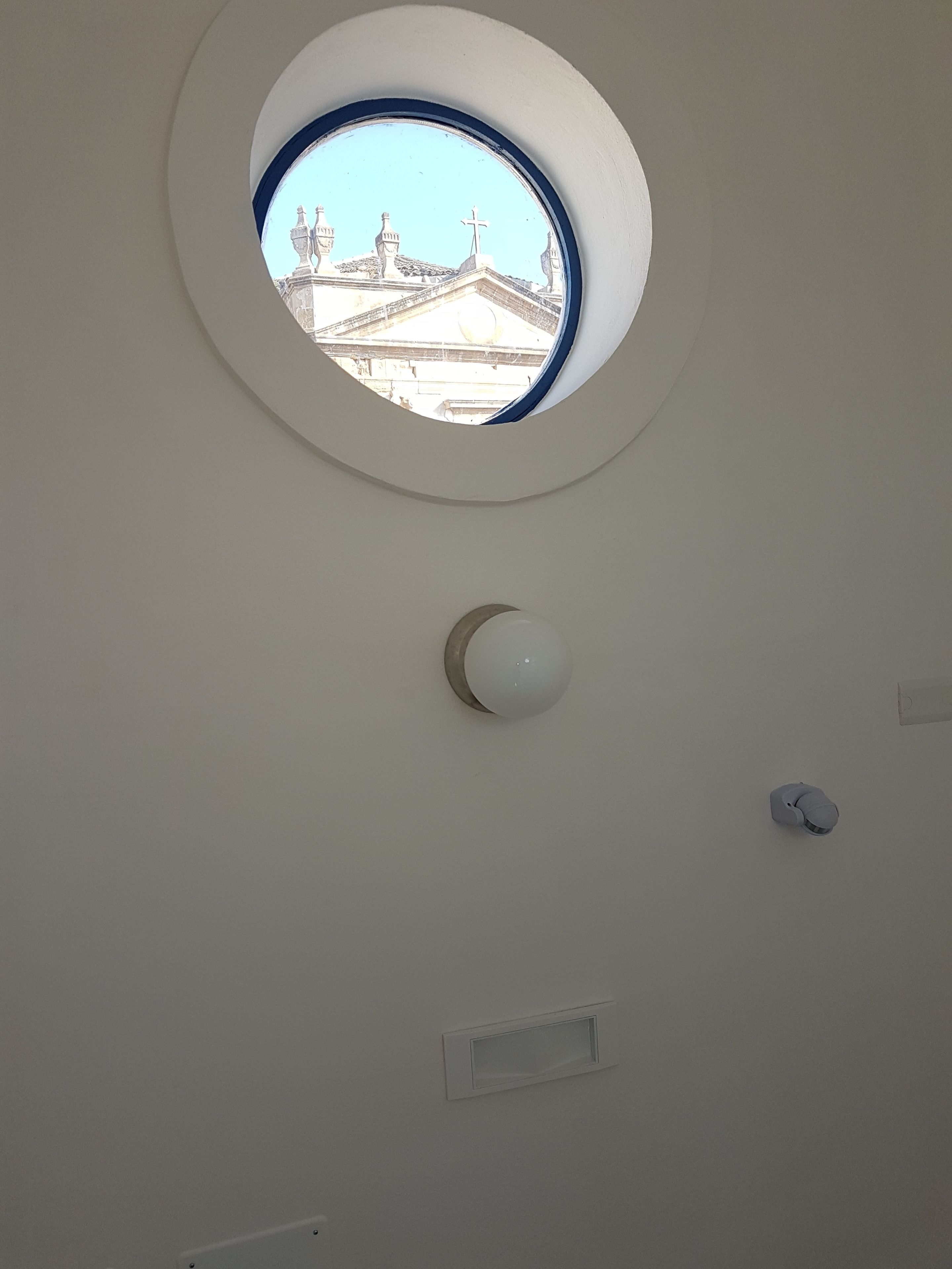 A circular window with a clear view of a building with a cross on top.