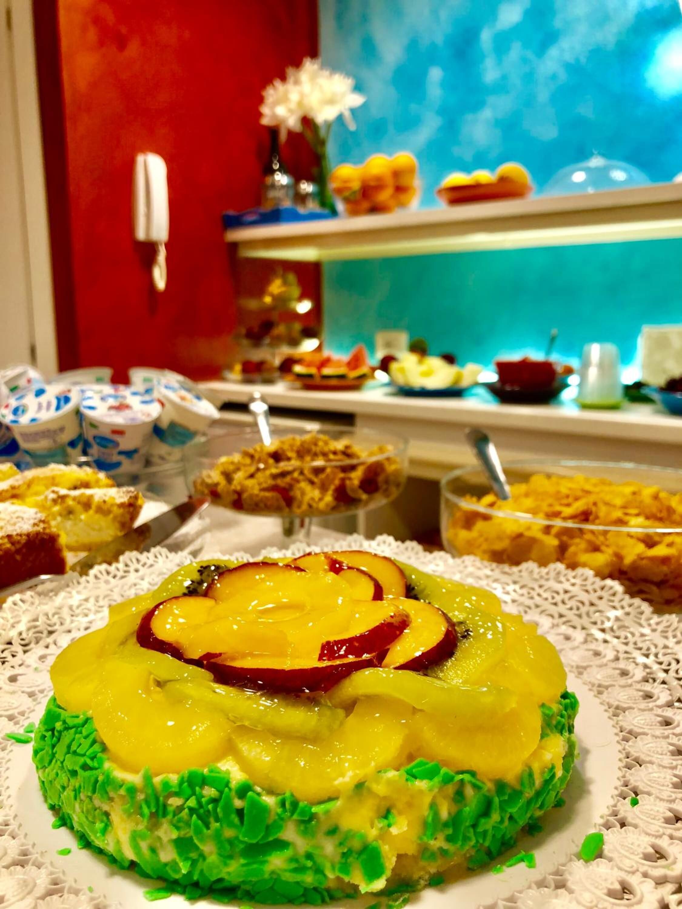 Un bufé con diversos platos, incluyendo un postre verde y amarillo con fruta por encima.