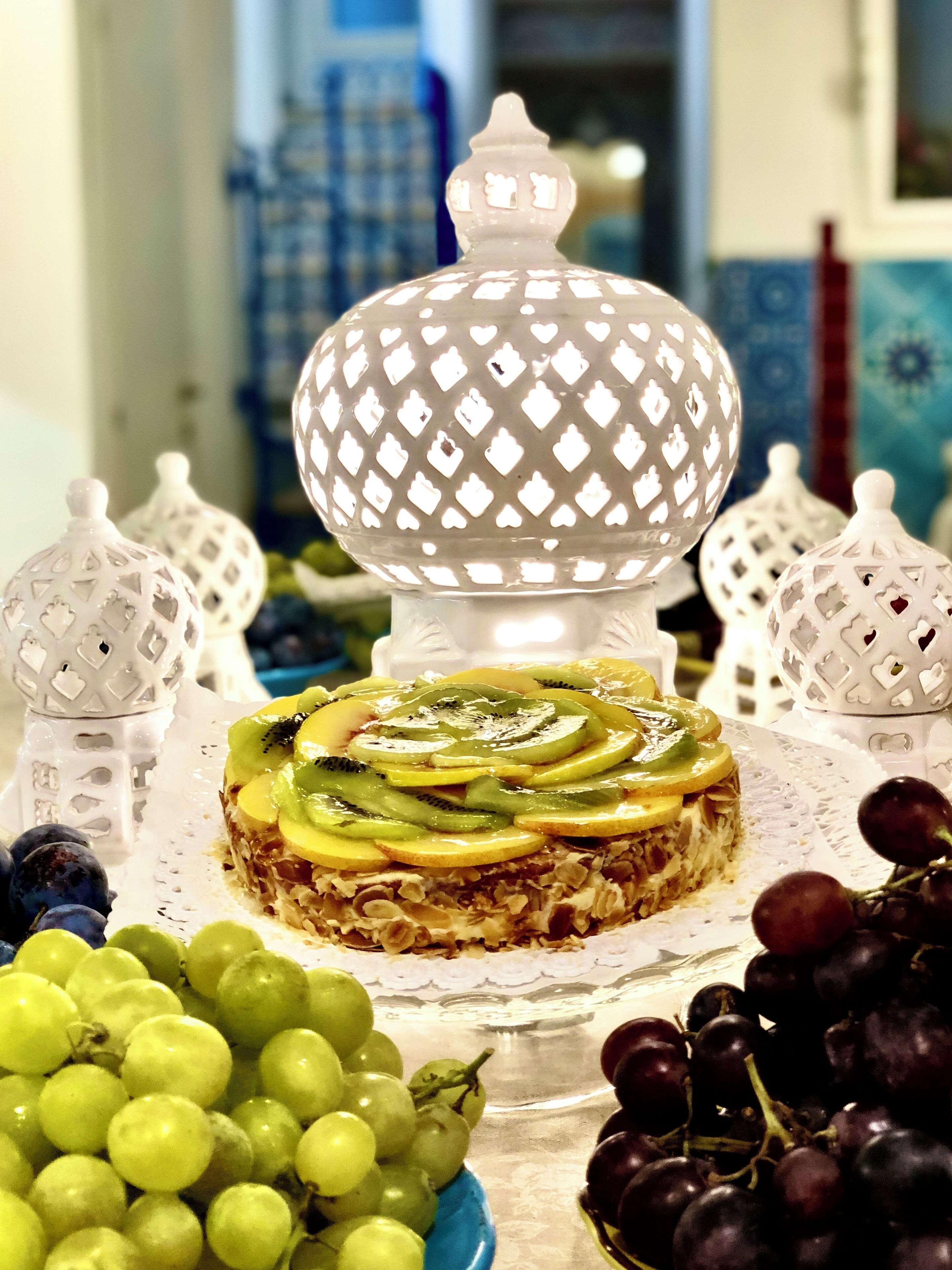 A dessert with fruit on a plate, surrounded by white decorative items and grapes.