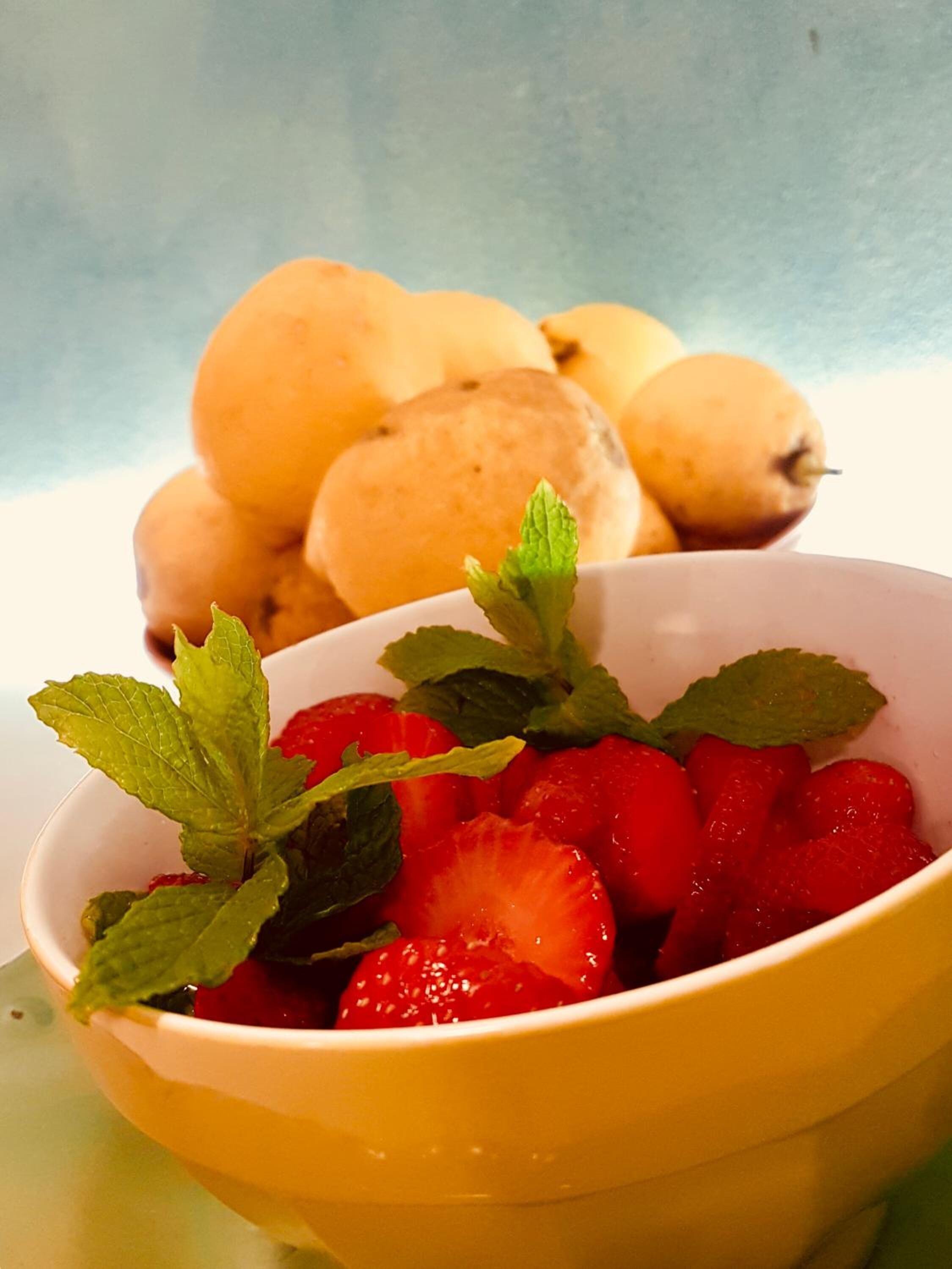 Un bol de fraises garni de feuilles de menthe, avec des poires en arrière-plan.