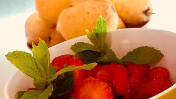 Un bol de fraises garni de feuilles de menthe, avec des poires en arrière-plan.