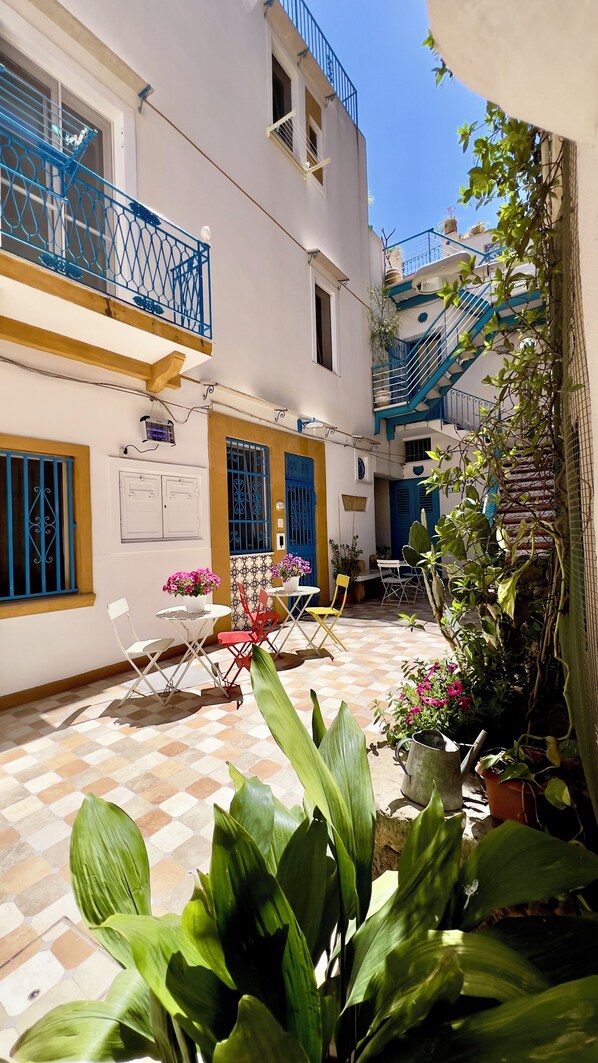 Un patio con suelo de baldosas, mobiliario exterior, plantas en macetas y una barandilla azul.