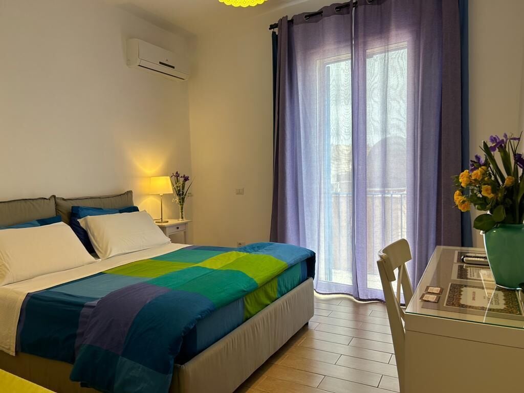 A bedroom with a bed, a nightstand, a lamp, a chair, and a table with a vase of flowers.