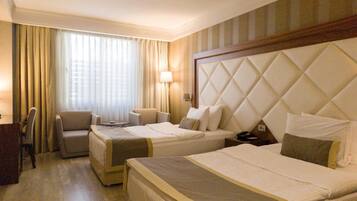 Quarto de hotel com duas camas, uma escrivaninha, uma cadeira e uma janela com cortinas.