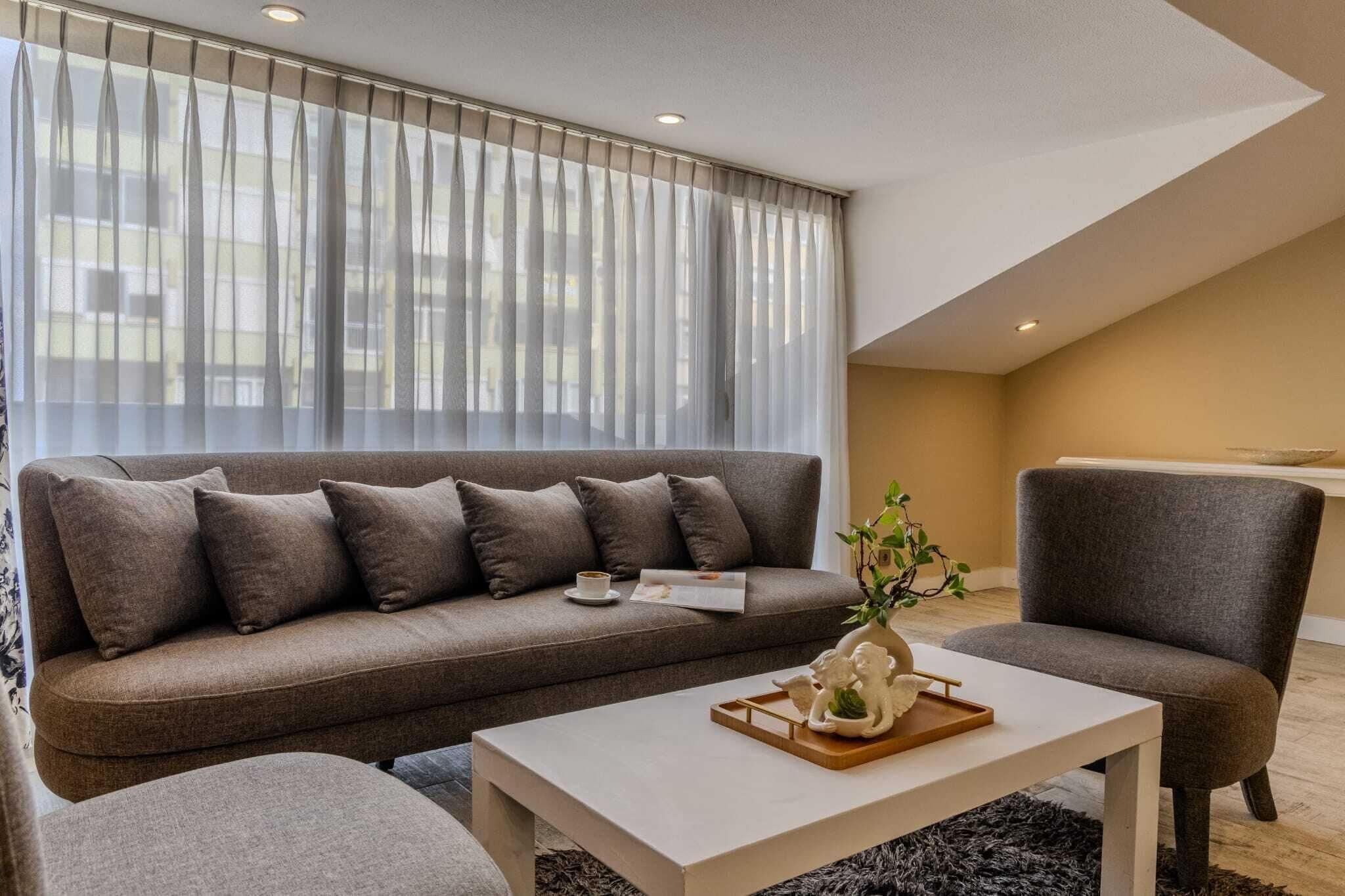 Een moderne woonkamer met een bank, fauteuil, salontafel en een raam met transparante gordijnen.