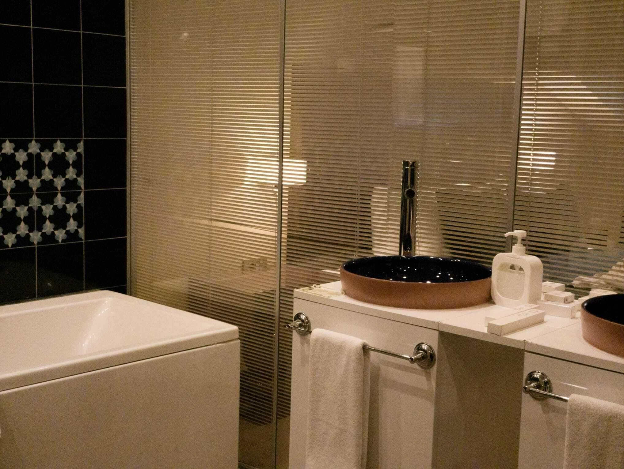 A bathroom with a white sink, a mirror, a towel rack, and a glass partition.