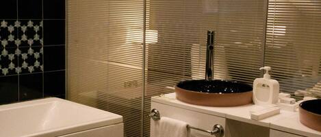A bathroom with a white sink, a mirror, a towel rack, and a glass partition.