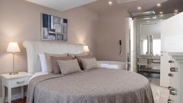 Un dormitorio con una cama grande, mesitas de noche, cabecero, una obra de arte colgada en la pared, y un baño visible a través de una puerta abierta.