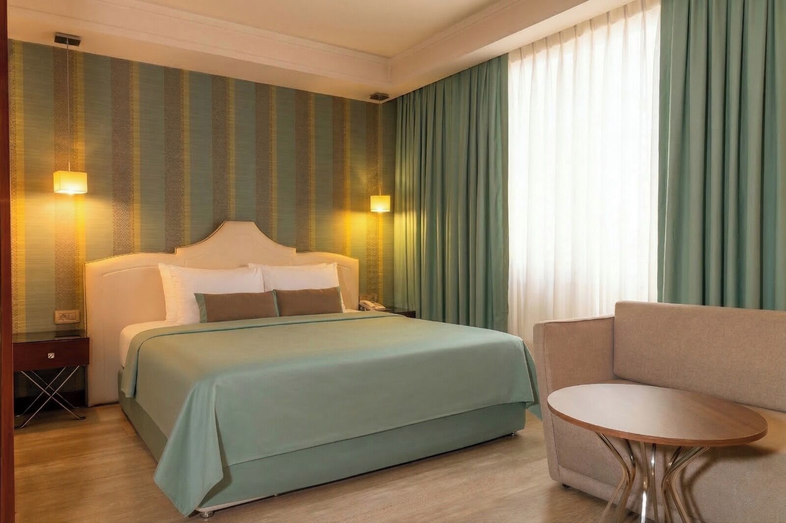 A hotel room with a bed, bedside table, lamp, and a small round table.