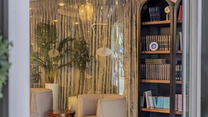 A room with a bookshelf, two armchairs, a small table, and a curtain with vertical lines. - Adana Plaza Otel (Adana)