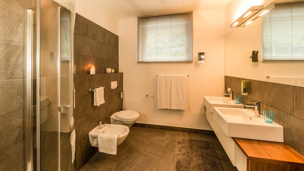 A modern bathroom with a glass shower enclosure, a toilet, and a vanity with two sinks.