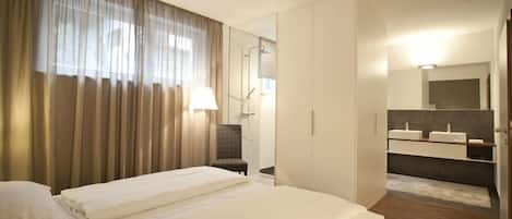 A hotel room with a bed, a chair, a bathroom with a mirror and sinks.