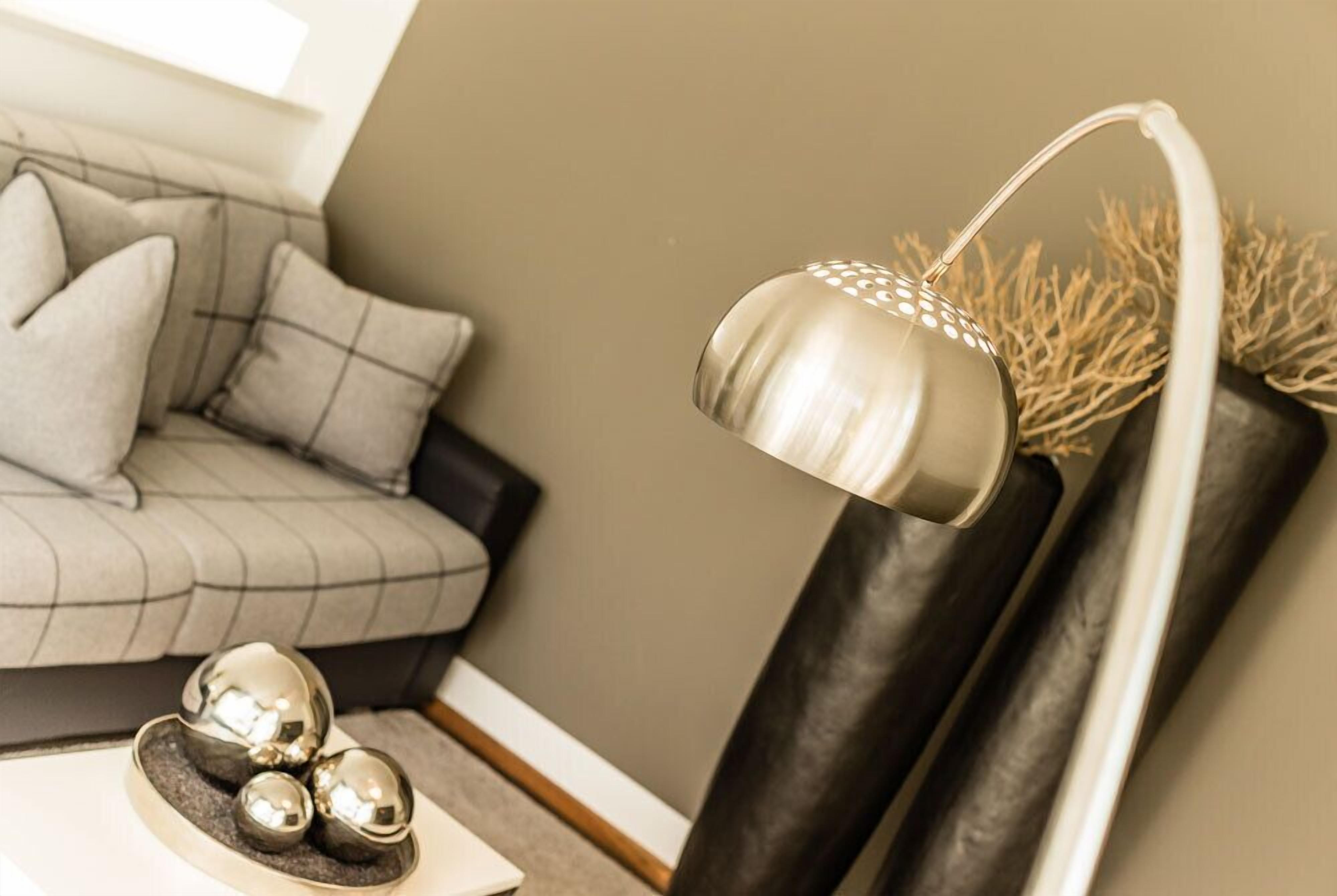 Een moderne woonkamer met een grijze bank, een witte salontafel met decoratieve bolvormen en een metalen vloerlamp.