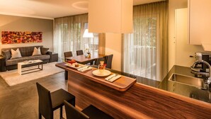 A modern hotel room with a dining area, a sofa, a coffee machine, and a large window with curtains. - Hidalgo Suites & Restaurant (Postal)