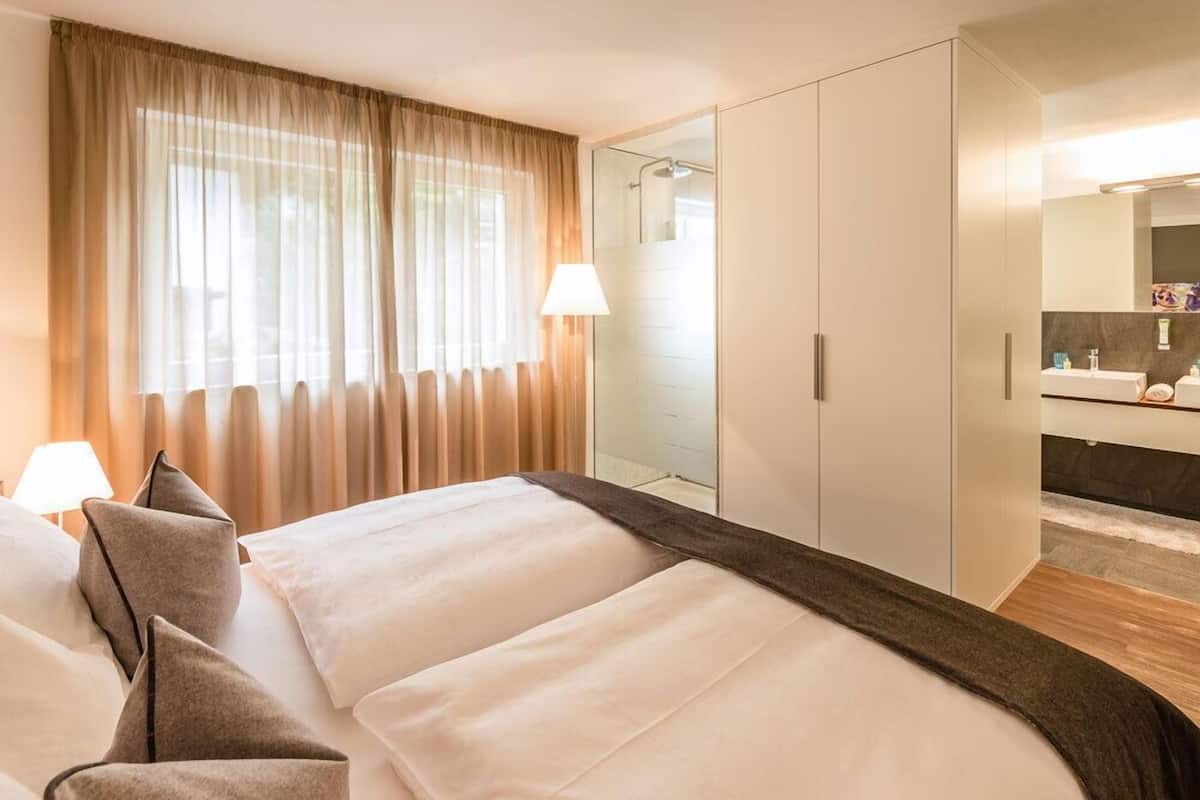 A hotel room with a bed, a large mirror, a wardrobe, and a bathroom with a sink and mirror.