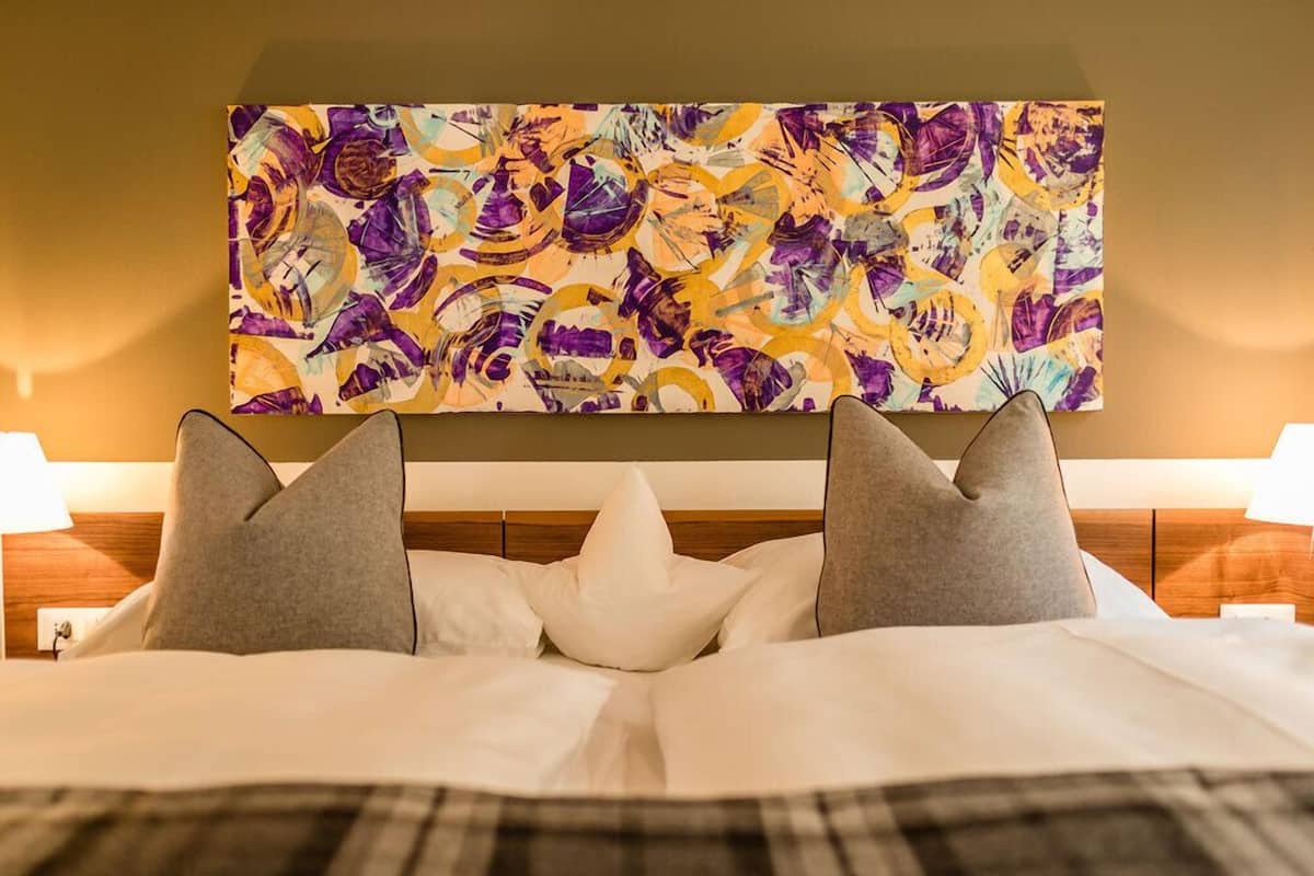A hotel room with a large abstract painting above the bed, a wooden headboard, and two bedside lamps.