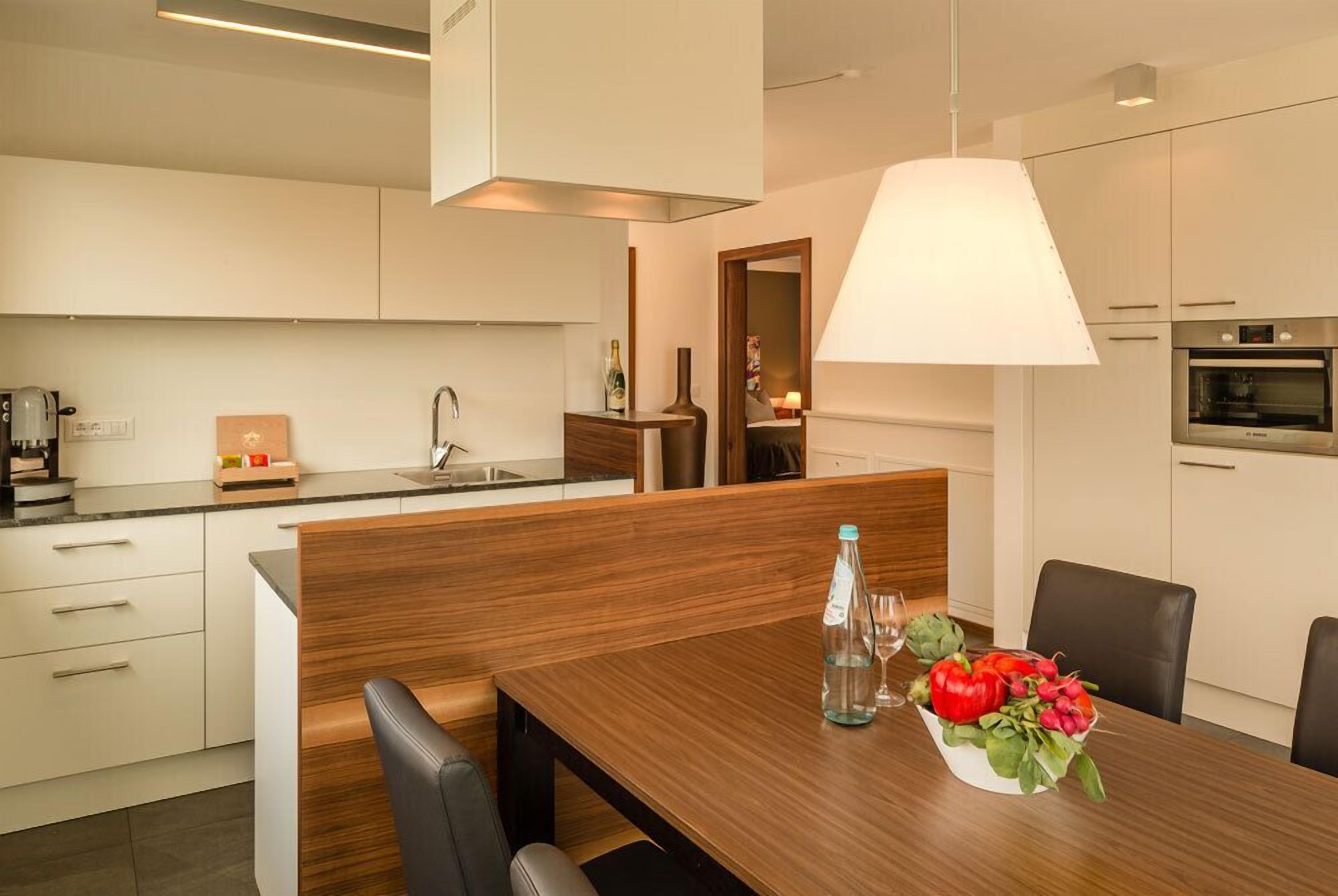 A modern kitchen with white cabinetry, a wooden dining table, and a pendant light.