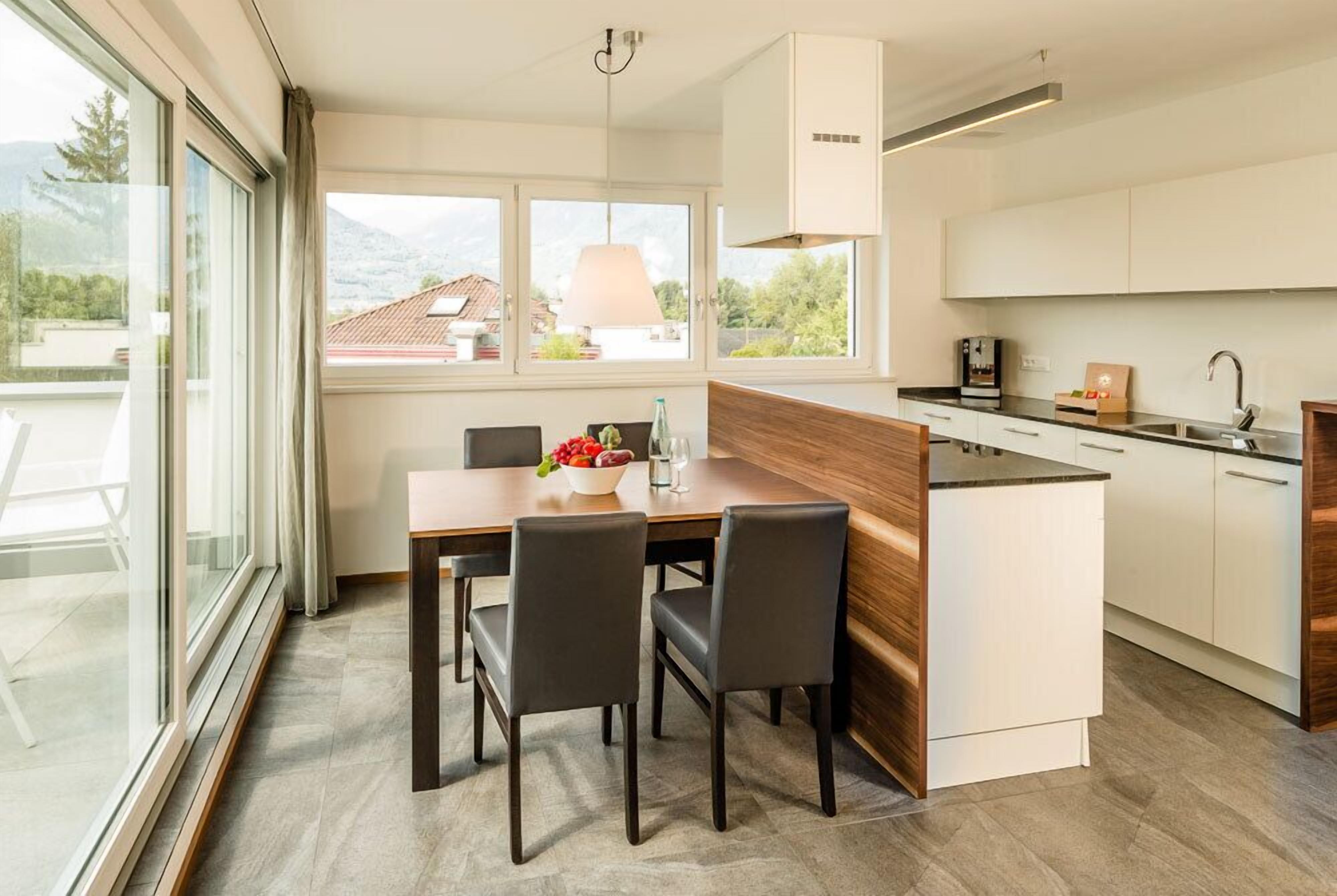 A modern kitchen with a dining area, large windows, and a view of the outdoors.