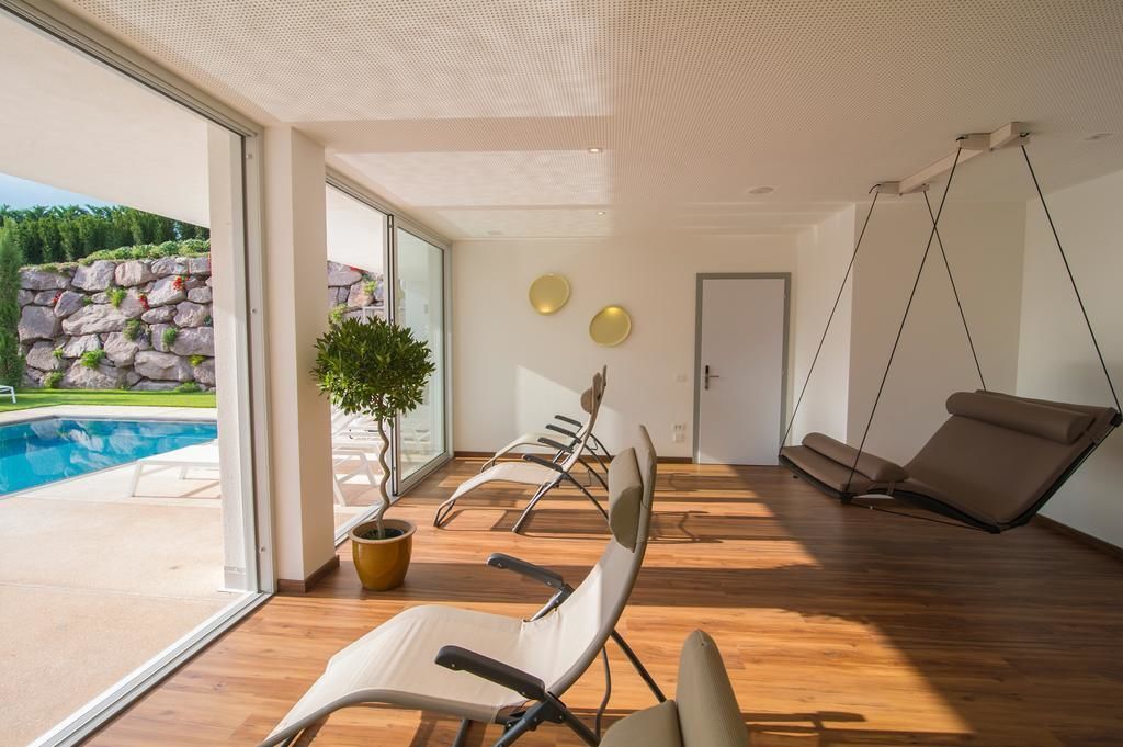 Ein modernes Zimmer mit Holzboden, einem großen Fenster, einer Topfpflanze und einem Schaukelstuhl.