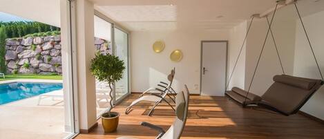 A modern room with a wooden floor, a large window, a potted plant, and a swing chair.