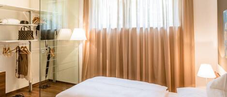 Una habitación de hotel con cama, armario de vidrio y ventana con cortinas.