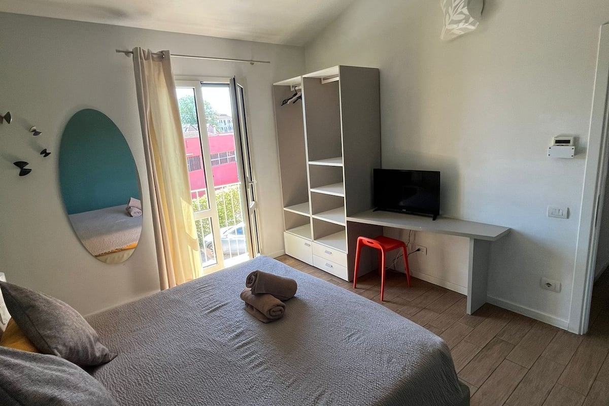 A bedroom with a bed, a desk, a TV, and a window with curtains.