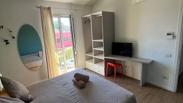 A bedroom with a bed, a desk, a TV, and a window with curtains.