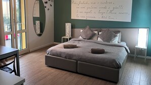 Un dormitorio con cama, mesitas de noche, un escritorio y un ventanal grande.