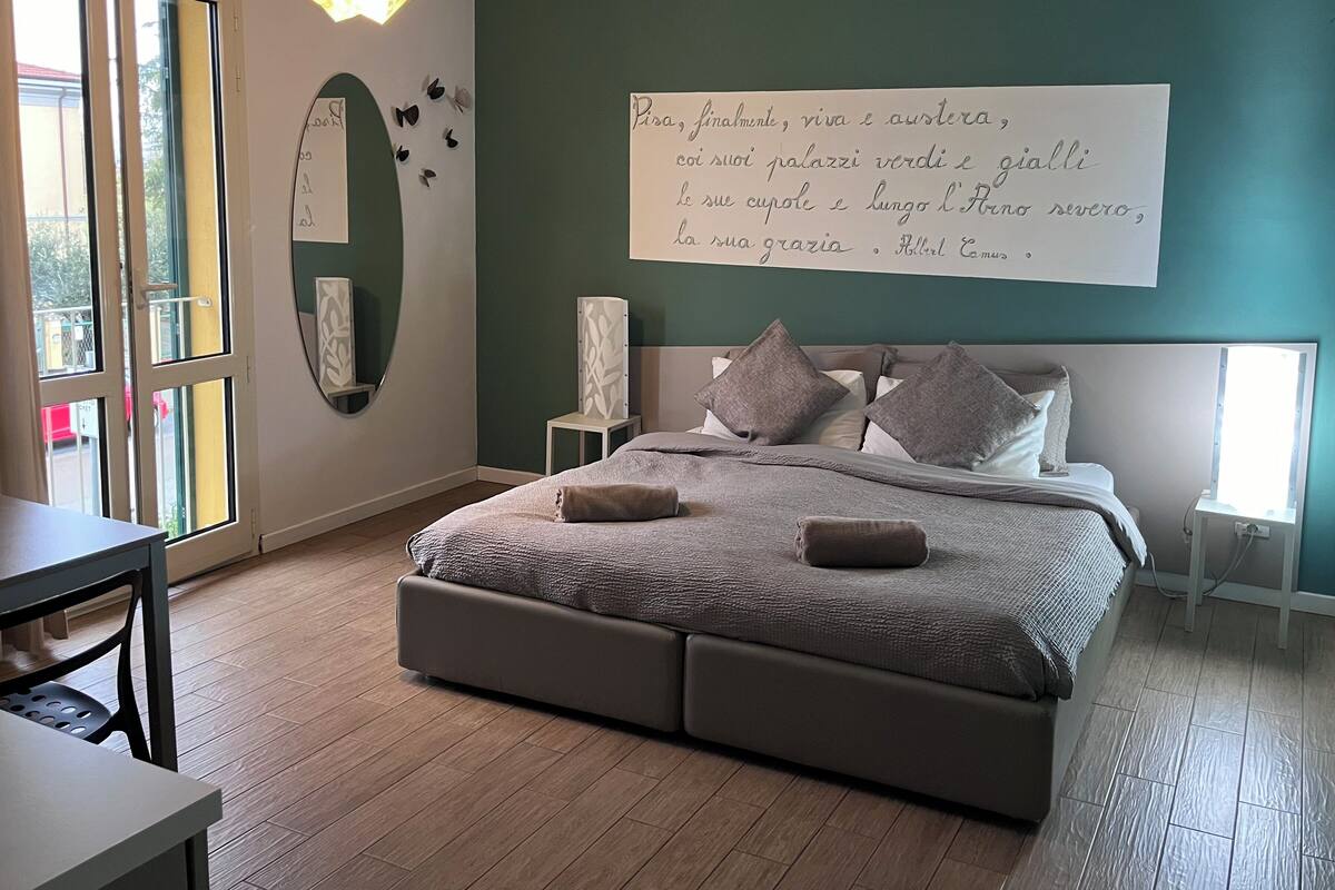 A bedroom with a bed, bedside tables, a desk, and a large window.
