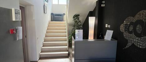 Un interior moderno con una escalera que lleva a un nivel superior, un mostrador de recepción y una obra de arte en la pared.