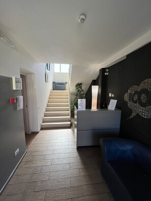 A modern interior with a staircase leading to an upper level, a reception desk, and a wall-mounted artwork. - Vele Storiche Pisane  (Pisa)