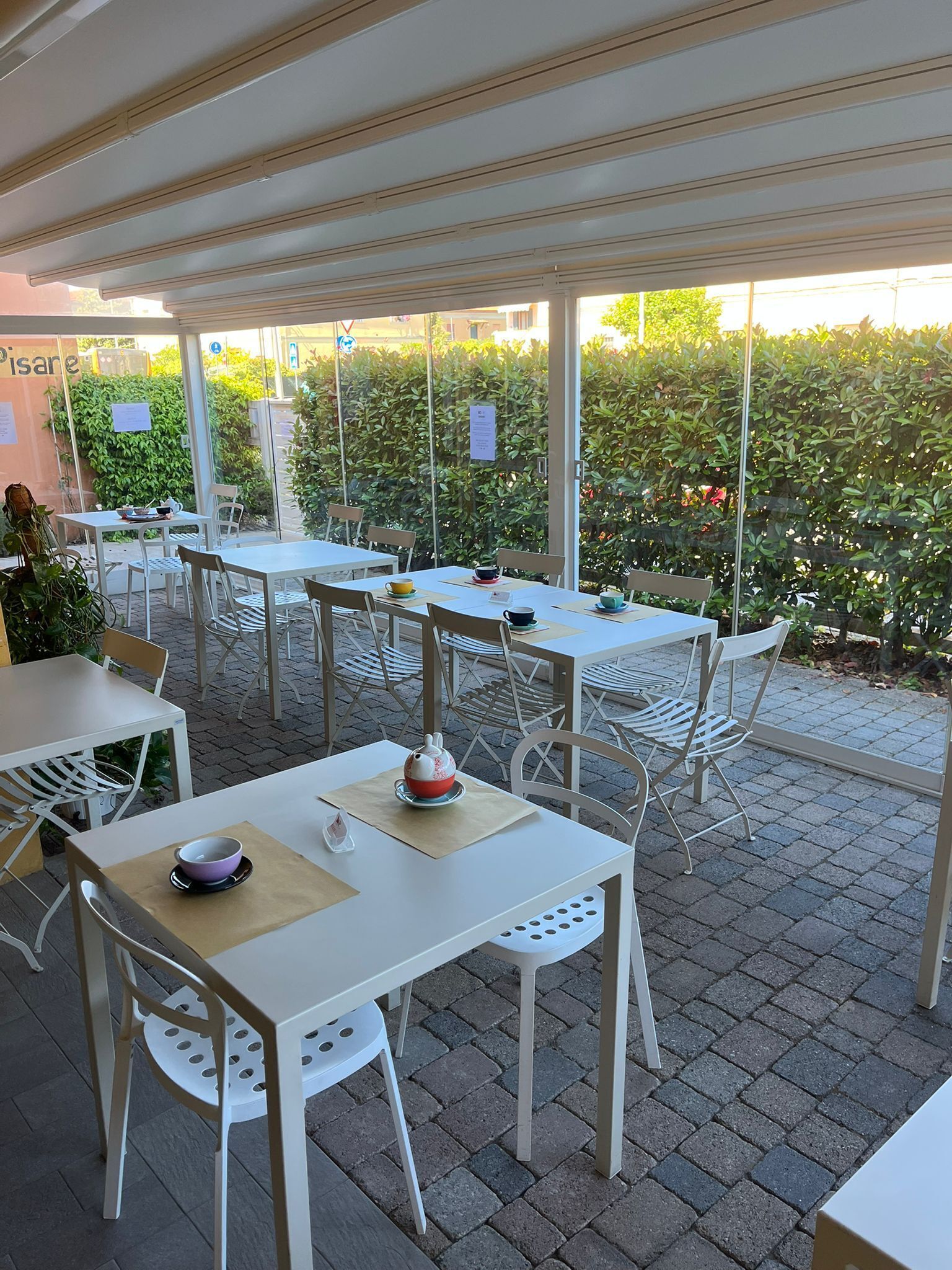 Un café al aire libre con mesas y sillas, una vista despejada del entorno verde y un letrero con el nombre del café.