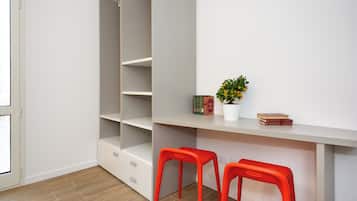 A room with a white desk, two red stools, a potted plant, and a bookshelf.