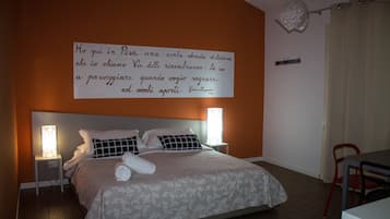 Ein ordentlich gemachtes Bett mit einem gemusterten Bettbezug und Kissen, einer Nachttischlampe sowie einer Wand mit einem Zitat auf Italienisch.