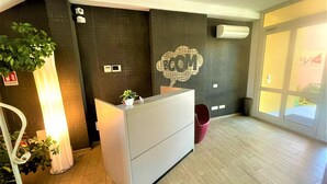 Zona de recepción con mostrador, aire acondicionado de pared, planta en maceta y un gran ventanal con vistas.