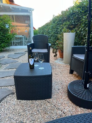 Outdoor wicker furniture with a bottle and glasses, a large planter, and a building with a sign in the background. - Vele Storiche Pisane  (Pisa)