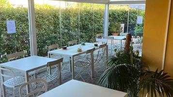 Un espace extérieur aménagé en terrasse, avec des tables et des chaises, un pot de fleurs et une vue sur une haie.