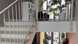 Un interior de varios niveles con una escalera, un balcón con plantas en macetas y vistas al exterior.