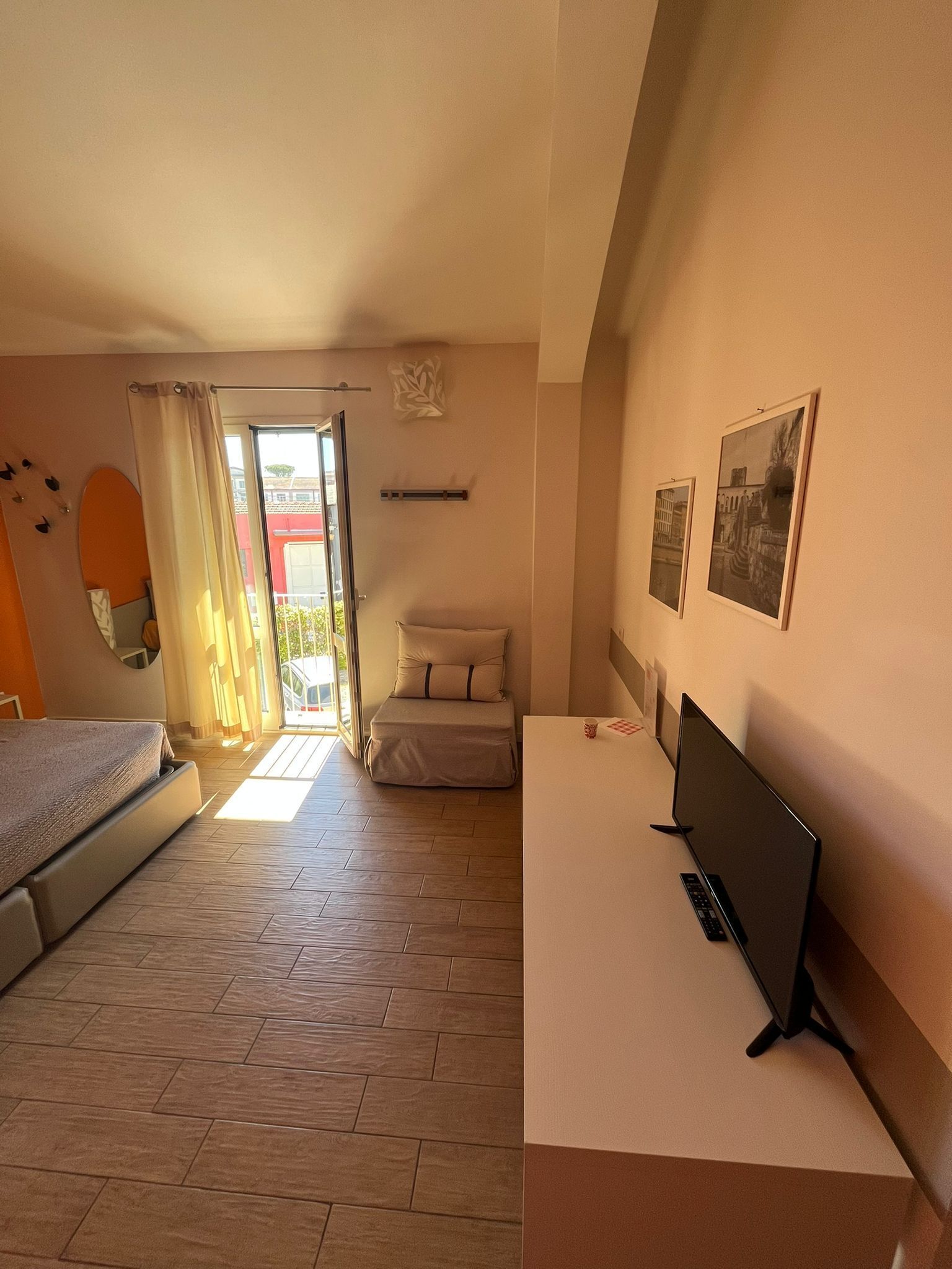 A bedroom with a bed, a desk with a computer, a chair, a window with curtains, and a door leading outside.